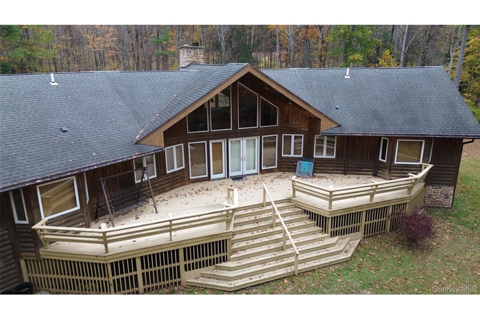 Rear view of house featuring a deck, a chimney, french doors, and log veneer siding