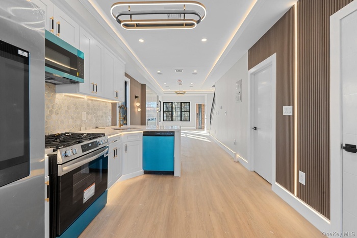 Kitchen featuring appliances with stainless steel finishes, white cabinets, backsplash, light wood-type flooring, and a peninsula
