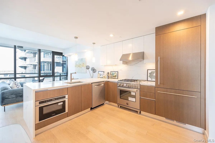 Kitchen with under cabinet range hood, appliances with stainless steel finishes, a peninsula, light wood-style floors, and a sink