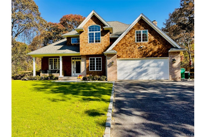 View of front of home featuring a chimney, covered porch, a front lawn, driveway, and a shingled roof