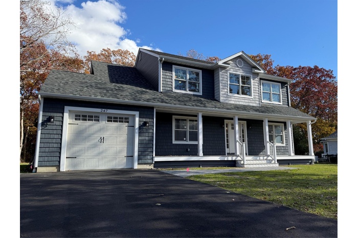 View of front of home with an attached garage, covered porch, a front yard, asphalt driveway, and roof with shingles