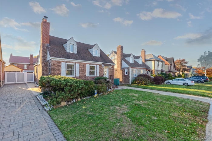 Cape cod home with a front yard, a chimney, brick siding, and a shingled roof