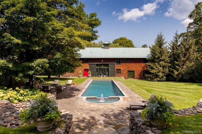 Rear view of house featuring a metal roof, a lawn, a patio, a pool with connected hot tub, and brick siding