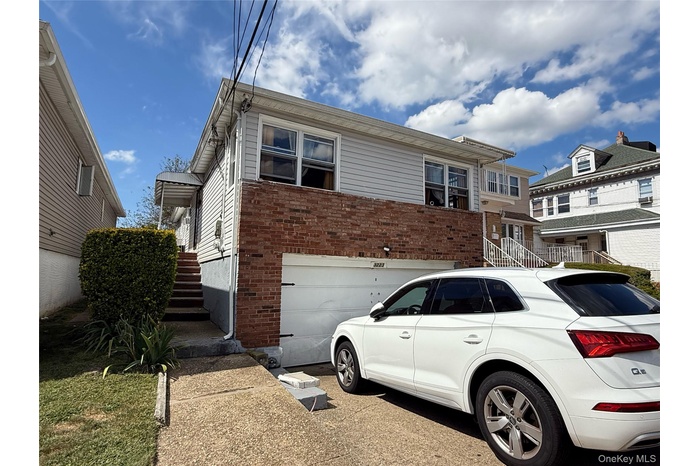 View of front facade featuring brick siding, driveway, a garage, and stairs