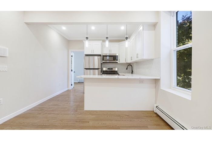Kitchen featuring tasteful backsplash, a baseboard radiator, white cabinets, light stone counters, and pendant lighting