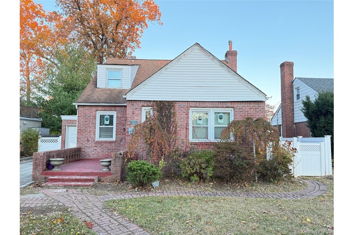 View of front facade with brick siding, a wooden deck, roof with shingles, and a chimney