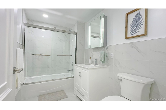 Full bathroom with vanity, bath / shower combo with glass door, and tile walls
