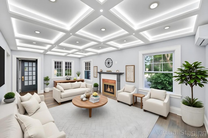 Living area featuring wood finished floors, healthy amount of natural light, a glass covered fireplace, coffered ceiling, and a wall mounted AC