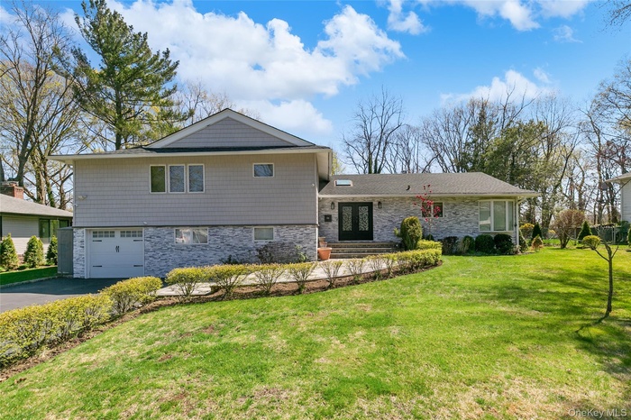 View of front of house featuring a front yard, a garage, asphalt driveway, and stone siding