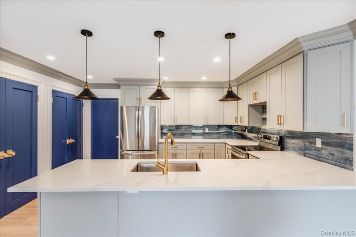 Kitchen with appliances with stainless steel finishes, a peninsula, light stone counters, decorative backsplash, and hanging light fixtures