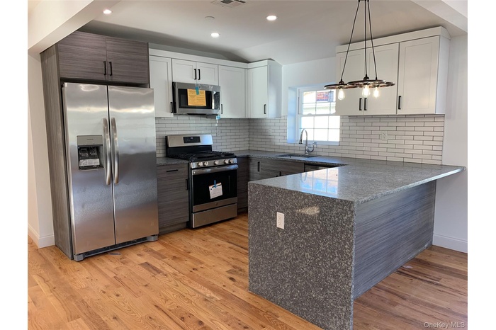 Kitchen featuring dark stone countertops, stainless steel appliances, backsplash, white cabinetry, and a peninsula