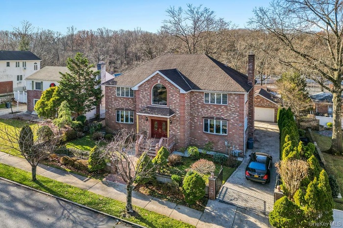 Traditional home featuring a chimney, decorative driveway, brick siding, and roof with shingles
