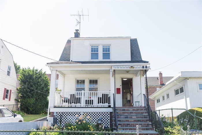 View of front of home featuring covered porch, a fenced front yard, roof with shingles, a chimney, and stairs