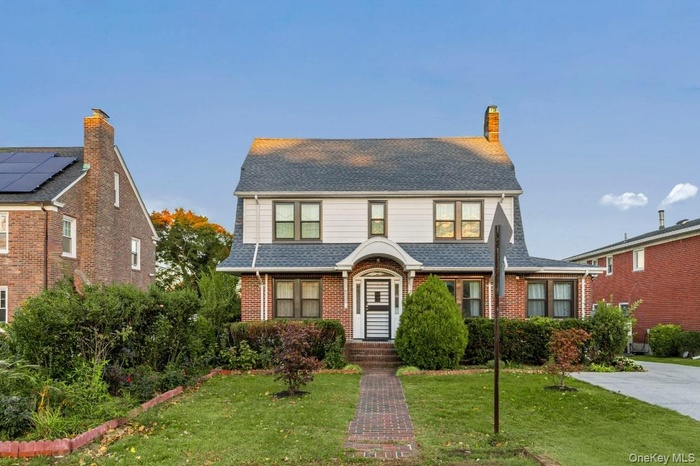 View of front of property with a front lawn, brick siding, a shingled roof, and a chimney