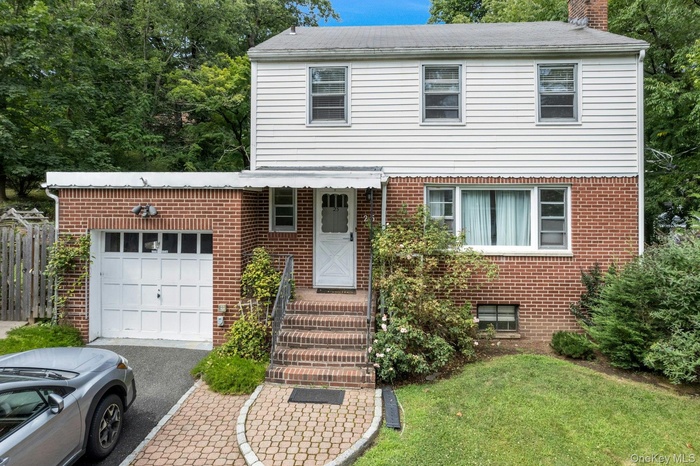 View of front of house with a chimney, brick siding, an attached garage, and asphalt driveway
