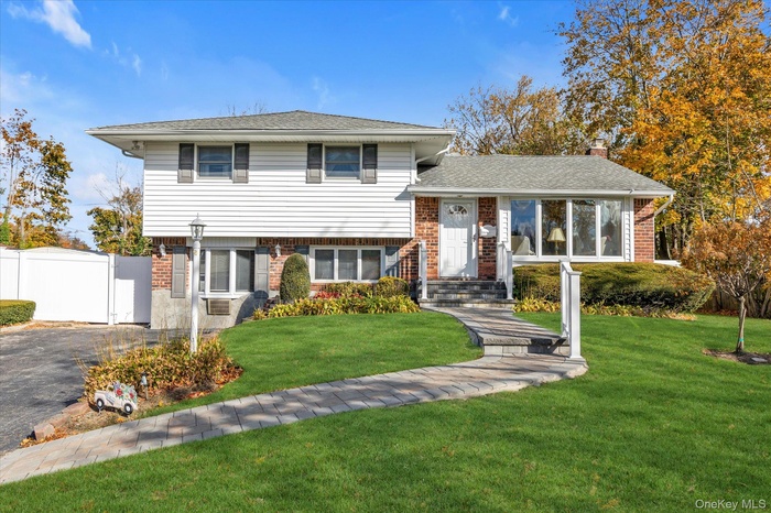 Split level home with brick siding, a gate, a shingled roof, and a chimney