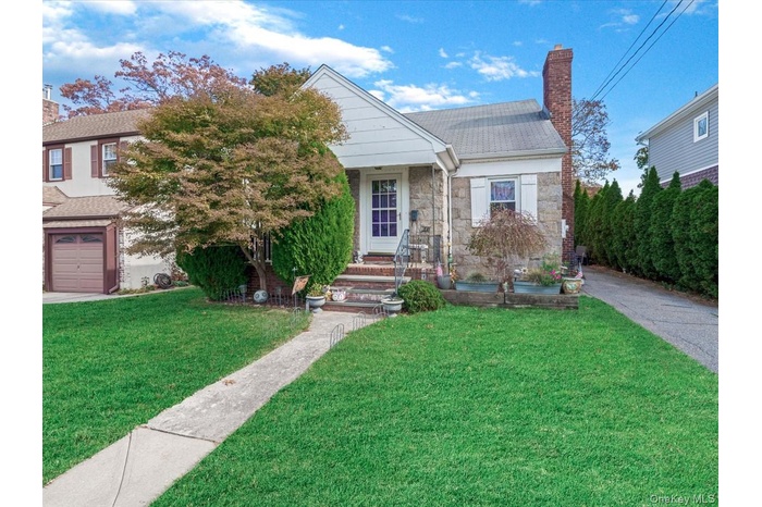 Bungalow-style house featuring a chimney, a front yard, stone siding, a shingled roof, and an attached garage