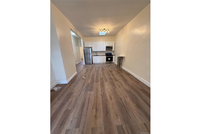 Unfurnished living room featuring baseboards and dark wood-type flooring