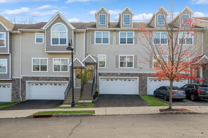 View of front facade with stone siding, driveway, and an attached garage