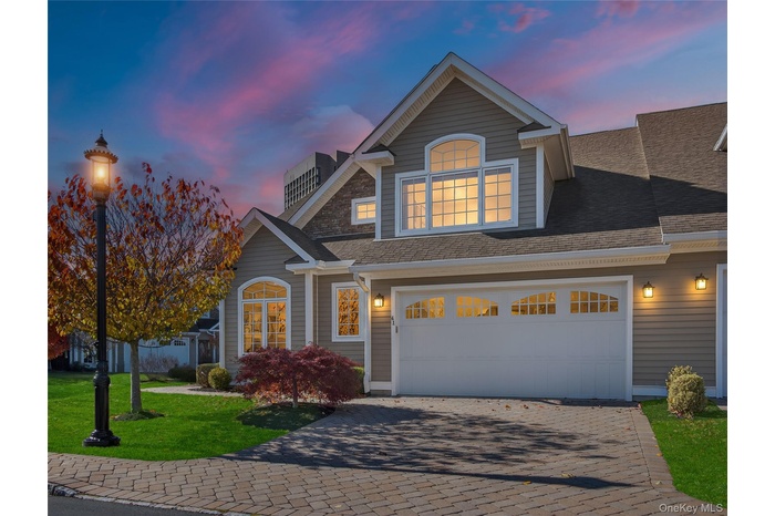 View of front of property with decorative driveway, a front lawn, a shingled roof, and a garage
