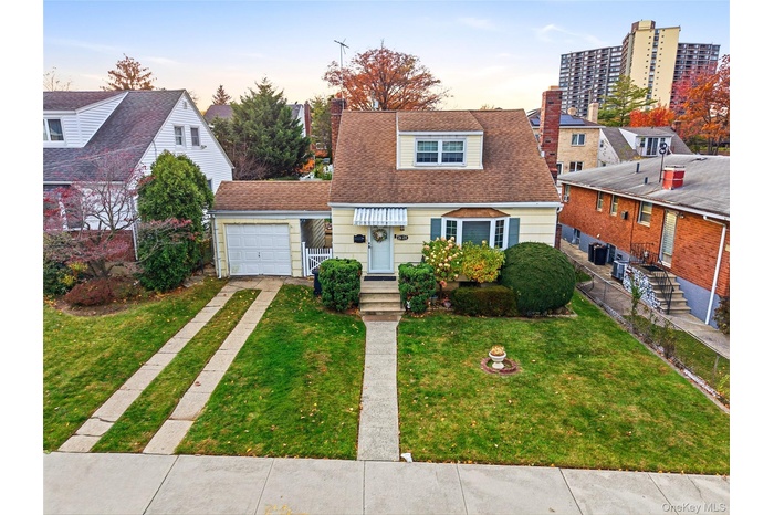 View of front of home featuring a shingled roof, a lawn, a chimney, a garage, and driveway