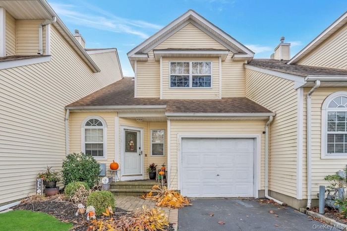 Traditional-style home featuring roof with shingles, driveway, and an attached garage