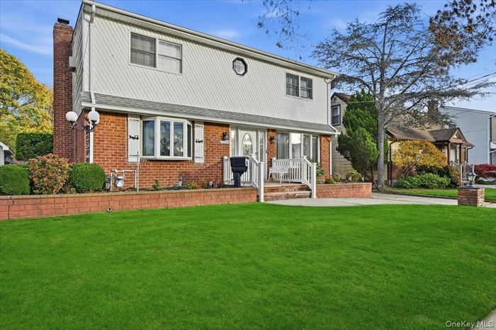 Colonial-style house featuring a chimney, a front yard, and brick siding