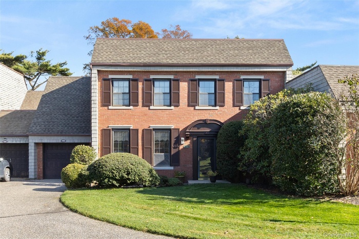 Colonial-style house featuring a front lawn, brick siding, an attached garage, a shingled roof, and driveway