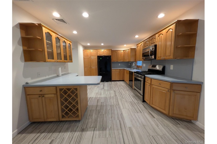 Kitchen with open shelves, glass insert cabinets, black appliances, wine storage cabinet, light countertops &  back-splash, and recessed lighting.