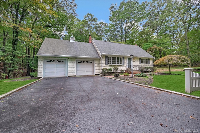 View of front of property featuring asphalt driveway, roof with shingles, a front lawn, and a chimney