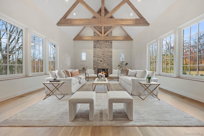 Living Room featuring custom wood beams, high ceiling, wall of windows, ceiling fan and stone fireplace