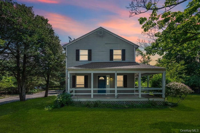 Back of house at dusk with a lawn, a porch, and a shingled roof