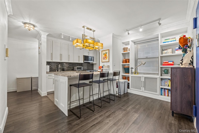 Kitchen featuring a kitchen bar, rail lighting, ornamental molding, backsplash, and light stone counters