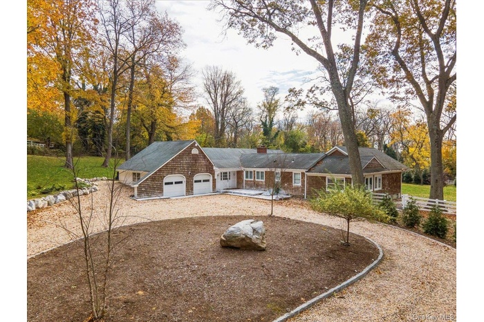 View of front of property featuring driveway, a chimney, an attached garage, and view of scattered trees