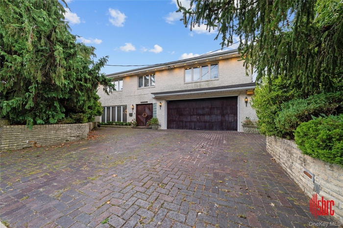 View of front of property featuring decorative driveway, brick siding, and a garage