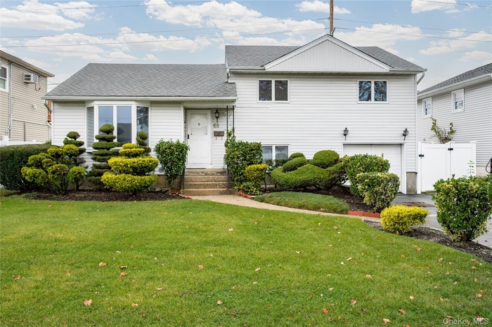 Split level home featuring a shingled roof, a front lawn, and an attached garage