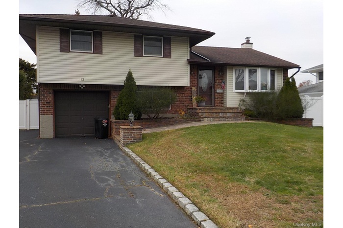 Tri-level home with brick siding, an attached garage, driveway, a chimney, and roof with shingles