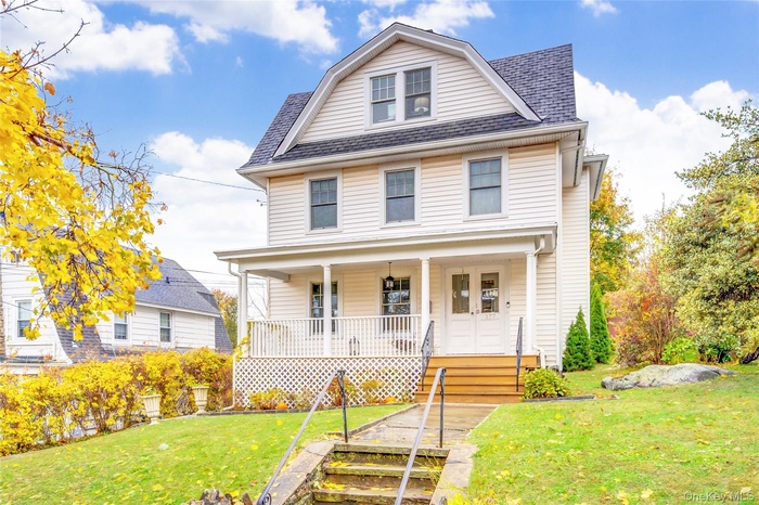 View of front facade featuring a porch, a front yard, roof with shingles, and a gambrel roof