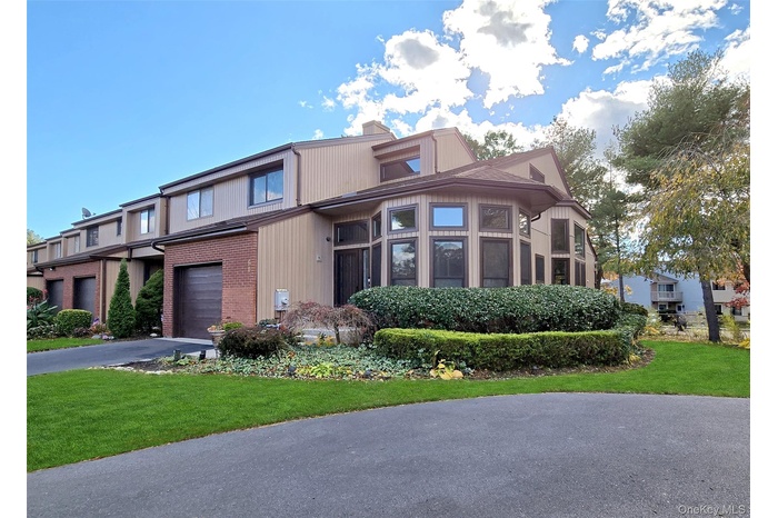 View of front of home with asphalt driveway, brick siding, a garage, a chimney, and a front yard