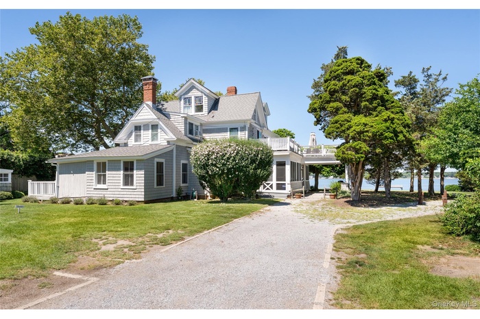 View of front facade with a balcony, a chimney, a front yard, gravel driveway, and a shingled roof