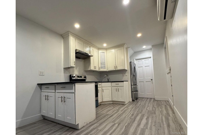 Kitchen with dark countertops, stainless steel appliances, light wood-style floors, recessed lighting, and white cabinets