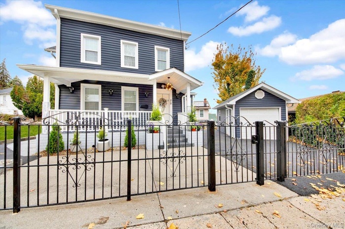 View of front facade with an outbuilding, a porch, a gate, a fenced front yard, and a detached garage