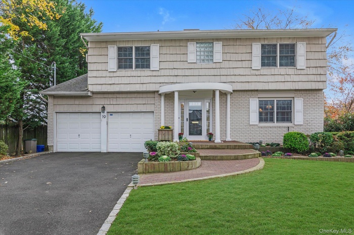 Colonial inspired home featuring driveway, a garage, a front lawn, and brick siding
