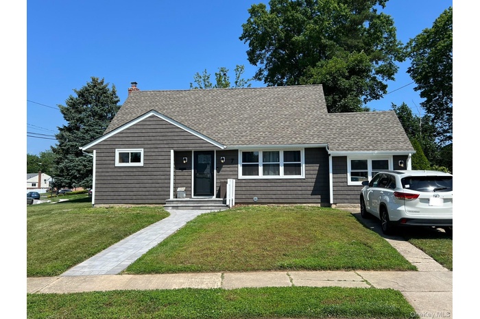 View of front of home featuring roof with shingles, a front yard, and a chimney