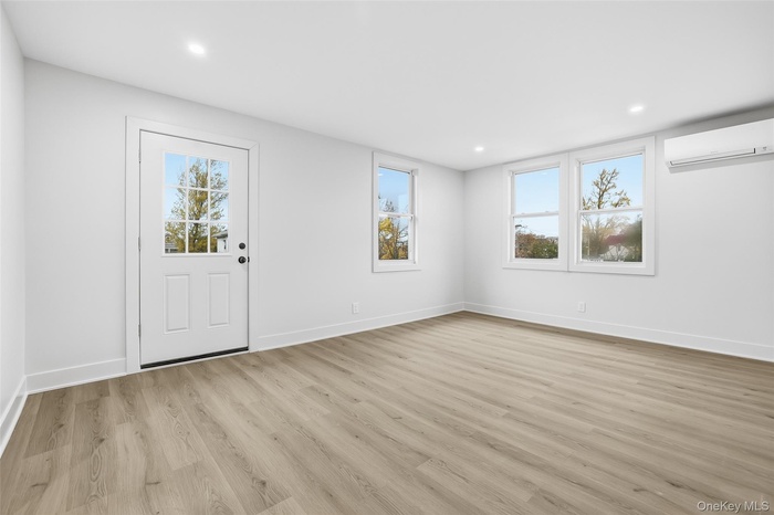 Foyer with healthy amount of natural light, light wood finished floors, an AC wall unit, and recessed lighting