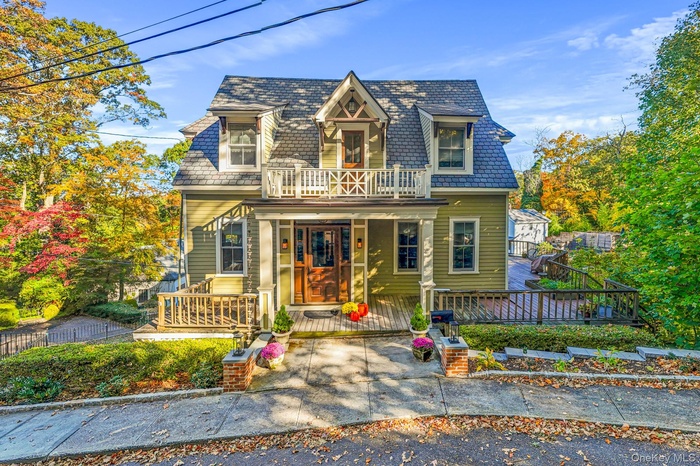 View of front facade with a high end roof, mansard roof, a balcony, and covered porch
