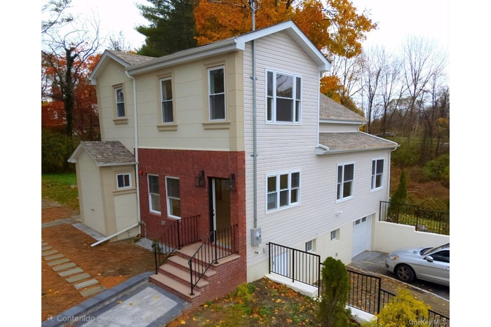 Back of property featuring a shingled roof, an attached garage, brick siding, and driveway