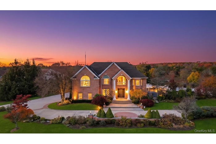View of front facade with a yard, curved driveway, and brick siding