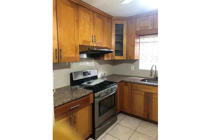 Kitchen featuring gas range, brown cabinets, under cabinet range hood, dark stone counters, and light tile patterned flooring
