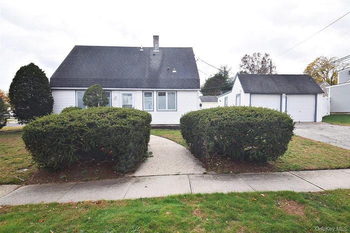 View of front of home with an outbuilding, a garage, roof with shingles, a front lawn, and a chimney